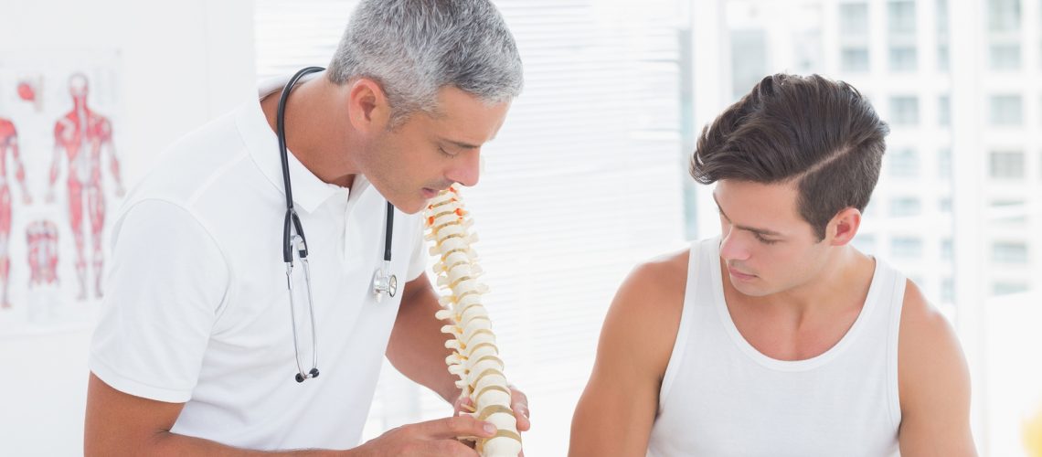 Doctor showing anatomical spine to his patient in medical office